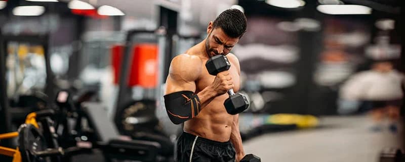 Man training with dumbbells while wearing an elbow support